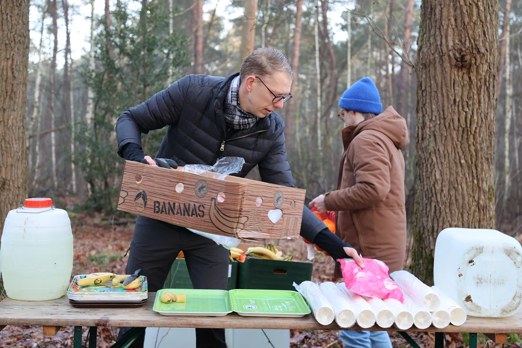 Twee vrijwilligers vullen de tafel van de verzorgingspost bij met bananen en bekers
