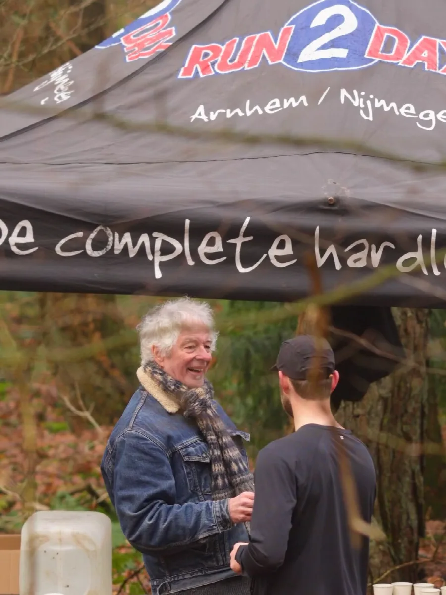 Vrijwilliger in spijkerjas geeft een loper een beker water aan bij de tent op de waterpost