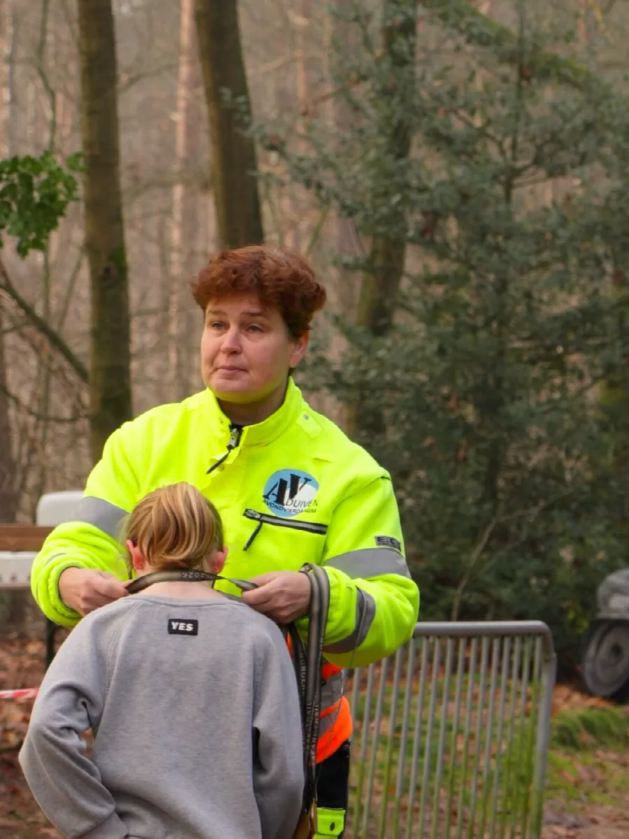 Vrijwilliger in geel hesje hangt een kind een medaille om aan de finish